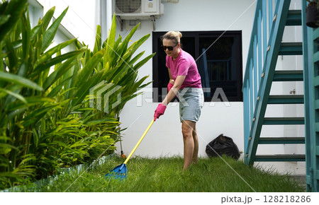 A woman raking the lawn at the backyard of her house A woman raking the lawn at the backyard of her house 128218286