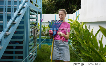 A woman raking the lawn at the backyard of her house  128218316