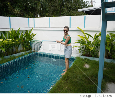 A young woman clean leaves out of a pool  128218320