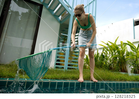 A young woman clean leaves out of a pool A young woman clean leaves out of a pool 128218325