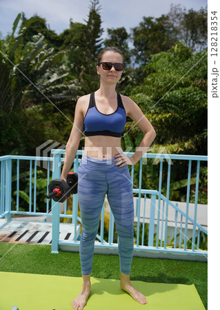 A young woman is training outdoors with dumbbells A young woman is training outdoors with dumbbells 128218354