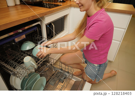 Young woman takes dishes out of the dishwasher machine Young woman takes dishes out of the dishwasher machine 128218403