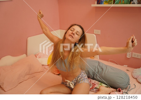 A young woman is enjoying a wonderfully serene morning in her bedroomnd  128218450