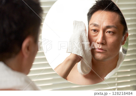鏡を見ながら顔を拭く中年男性 鏡を見ながら顔を拭く中年男性 128218484