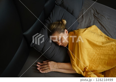 A woman sleeping peacefully under a yellow blanket A woman sleeping peacefully under a yellow blanket 128218499