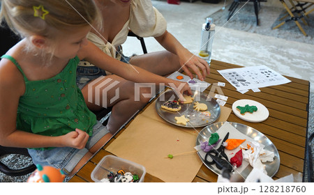 Mother and her daughter paint Halloween cookies  128218760