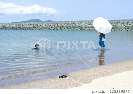 <素材>夏の海で子供が遊ぶ姿を見守る母 <素材>夏の海で子供が遊ぶ姿を見守る母 128219877