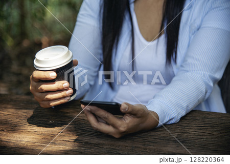 Woman drinking coffee hands holding hot disposable cup in green park. Happy Relax beautiful asian woman smiling face standing outdoors garden. Young women enjoy nature morning Freedom Lifestyle. Woman drinking coffee hands holding hot disposable cup in green park. Happy Relax beautiful asian woman smiling face standing outdoors garden. Young women enjoy nature morning Freedom Lifestyle. 128220364