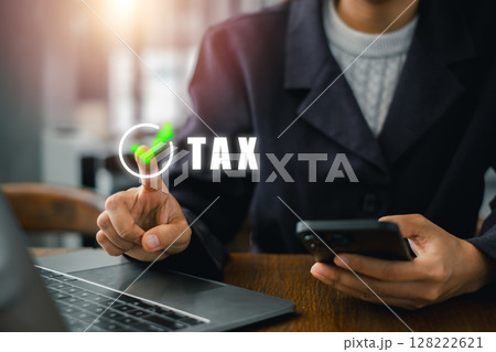 A business professional using a laptop and smartphone to manage taxes, highlighting modern financial technology. 128222621