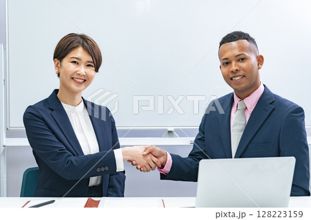ホワイトボードの前で握手する黒人男性ビジネスマンと日本人女性スタッフ 128223159