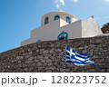 Greek flag waving in front of a traditional white and blue church in greece 128223752