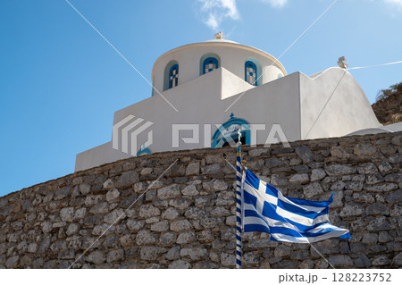 Greek flag waving in front of a traditional white and blue church in greece 128223752