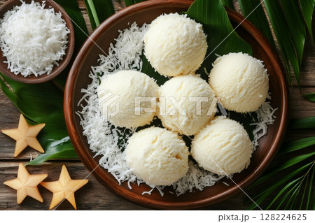 Creamy coconut ice cream scoops resting on wooden plate with shredded coconut and carambola slices 128224625