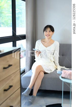 Pretty asian woman using smartphone on a sofa at home in a bright living room 128225306