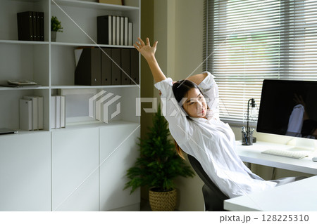 Young woman stretching and relaxing in chair after working at a computer in a bright office Young woman stretching and relaxing in chair after working at a computer in a bright office 128225310
