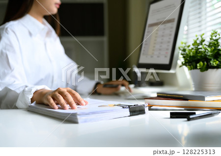 Businesswoman working with financial documents and computer data at a modern office desk 128225313