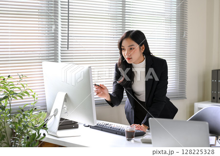 Focused businesswoman analyzing data on a computer screen while working in a bright office Focused businesswoman analyzing data on a computer screen while working in a bright office 128225328