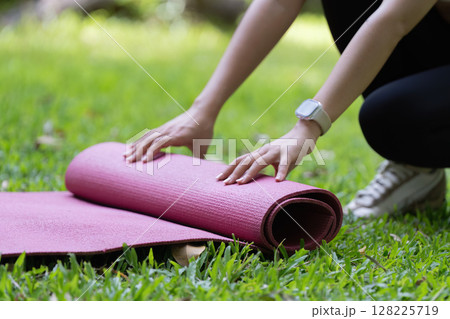 Yoga mat preparation. Close-up of hands rolling yoga mat on grass. 128225719