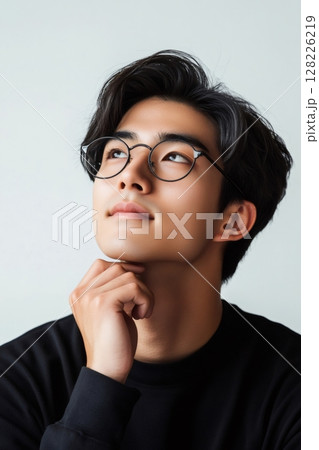 Pensive young man with glasses looking up and touching his chin Pensive young man with glasses looking up and touching his chin 128226219