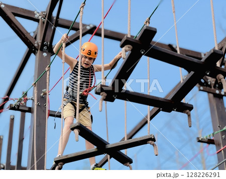 a teenage boy in outdoor rope park passing obstacle course. 128226291