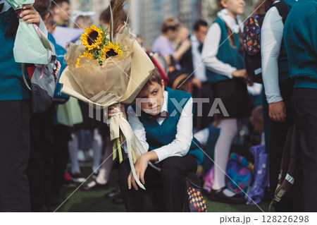 A 10-year-old boy carries a bouquet of flowers stressed before school on September 1st, dressed in formal attire with a backpack. A 10-year-old boy carries a bouquet of flowers stressed before school on September 1st, dressed in formal attire with a backpack. 128226298
