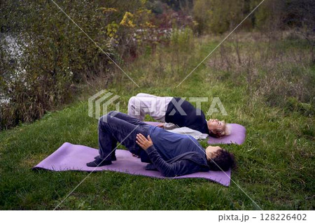 middle-aged woman teaches her old mother somatic exercises and yoga to maintain health by the river in autumn middle-aged woman teaches her old mother somatic exercises and yoga to maintain health by the river in autumn 128226402