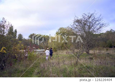 A middle-aged woman and her old mother take a morning jog together to maintain health by the river in autumn 128226404