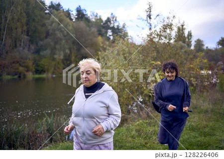 A middle-aged woman and her old mother take a morning jog together to maintain health by the river in autumn A middle-aged woman and her old mother take a morning jog together to maintain health by the river in autumn 128226406