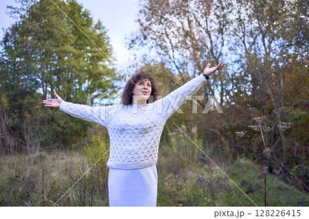middle-aged woman with dark curly hair in light beige suit enjoying nature in autumn forest middle-aged woman with dark curly hair in light beige suit enjoying nature in autumn forest 128226415