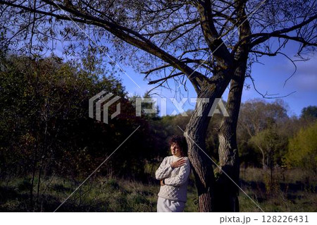 middle-aged woman with dark curly hair in light beige suit enjoying nature in autumn forest middle-aged woman with dark curly hair in light beige suit enjoying nature in autumn forest 128226431