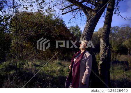 elderly woman with gray hair in light beige coat enjoying nature in autumn forest elderly woman with gray hair in light beige coat enjoying nature in autumn forest 128226440
