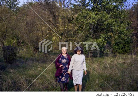 middle-aged daughter and elderly mother together on a walk in the autumn forest 128226455