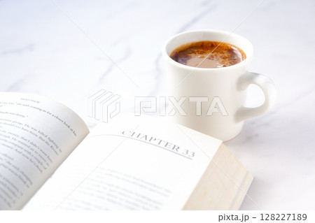 ペーパーバック（洋書）とコーヒーの入ったコーヒーカップで、コーヒーを飲みながら読書中のイメージ 128227189