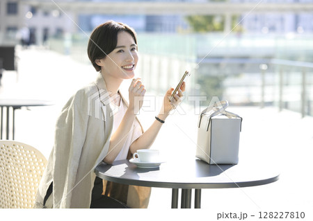 カフェテラスでスマートフォン見るリラックスした女性 カフェテラスでスマートフォン見るリラックスした女性 128227810