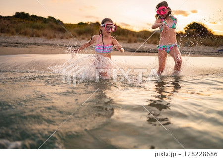Joyful moments of siblings playing in the gentle waves at sunset 128228686