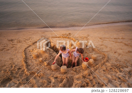Siblings build an elaborate sandcastle on a sunny beach afternoon Siblings build an elaborate sandcastle on a sunny beach afternoon 128228697