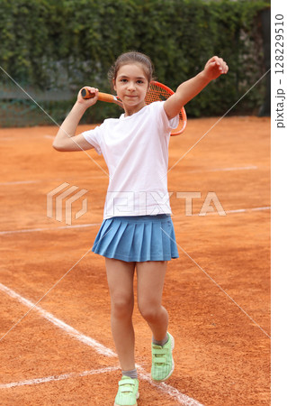Young girl playing tennis on a clay court showcasing skill and determination 128229510