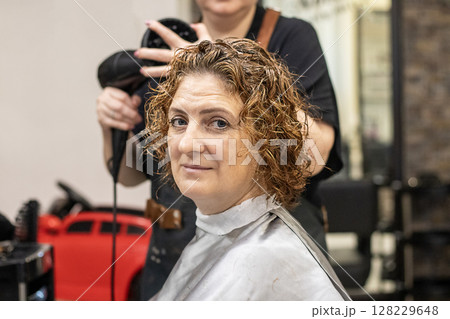 Woman receiving hair styling services at salon with a professional hairdresser 128229648