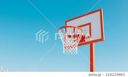 Basketball hoop under clear blue sky at outdoor court showcasing sports equipment and urban recreation facilities 128229963