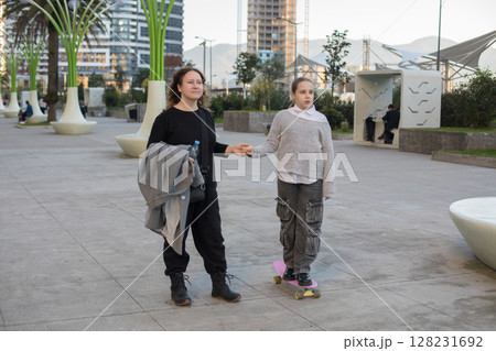 Happy mother and daughter skateboarder on pink skateboard. A child and an active hobby Happy mother and daughter skateboarder on pink skateboard. A child and an active hobby 128231692