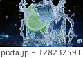 Fresh lime splashes into clear water creating ripples and droplets under soft lighting in a dark setting 128232591