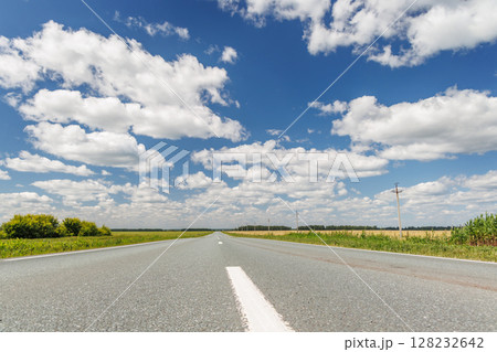 Endless asphalt road stretching through a summer landscape of green fields under a sunny sky 128232642