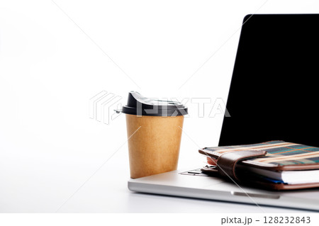 Closeup of an office table featuring a sleek laptop and a coffee cup on a clean white surface Closeup of an office table featuring a sleek laptop and a coffee cup on a clean white surface 128232843