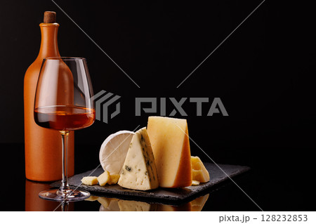 A refined selection of aged cheeses presented on a board, accompanied by a glasses of wine 128232853