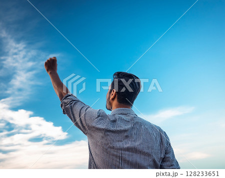 青空の下で手に持ったペンを高く上げる男性 128233651