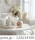 Adorable baby lying in a bright, white, sunlit bedroom surrounded by white flowers. Warm and serene atmosphere. Soft natural light, white linens, and floral decor enhance the gentle. 128234300