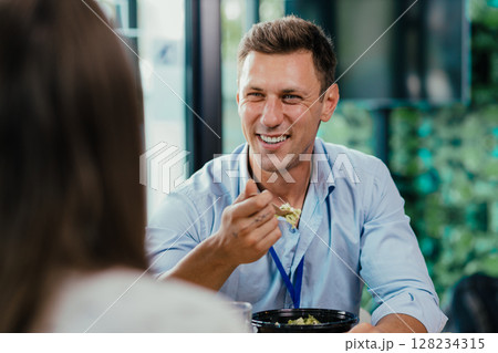 Young businessman eating healthy salad lunch with colleagues in modern office cafeteria Young businessman eating healthy salad lunch with colleagues in modern office cafeteria 128234315