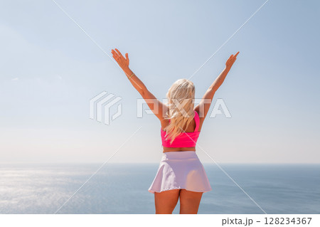 A woman in a pink top and white skirt is standing on a beach A woman in a pink top and white skirt is standing on a beach 128234367