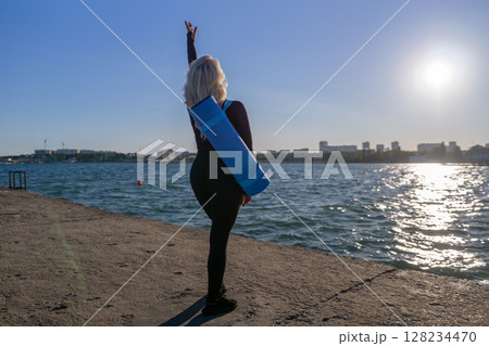 Yoga Woman Beach Sunrise Pose - Woman practicing yoga on a beach with a yoga mat at sunrise. Yoga Woman Beach Sunrise Pose - Woman practicing yoga on a beach with a yoga mat at sunrise. 128234470