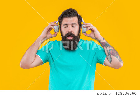 shocked annoyed man listen loud music in headphones. annoyed man in headphones with loud music. shocked annoyed man listen loud music in headphones. annoyed man in headphones with loud music. 128236360